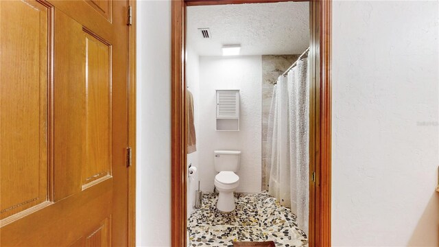 bathroom featuring toilet, a textured ceiling, and a shower with curtain