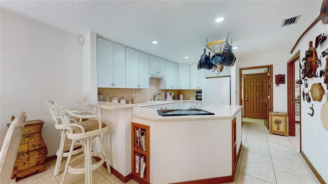 kitchen featuring white fridge, white cabinets, light tile patterned floors, kitchen peninsula, and gas stovetop