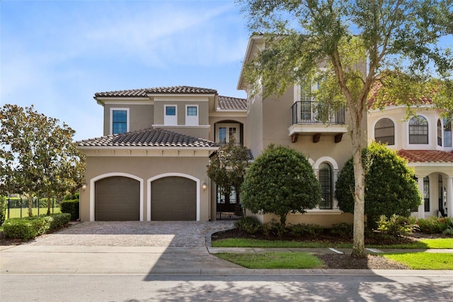 mediterranean / spanish house with a tile roof, stucco siding, decorative driveway, a garage, and a balcony