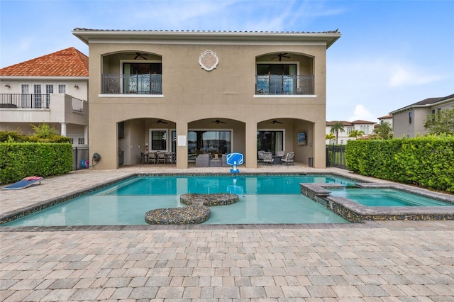 back of property with a balcony, ceiling fan, a patio area, and a swimming pool with hot tub