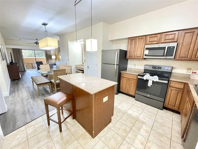 kitchen with ceiling fan, light wood-type flooring, hanging light fixtures, a breakfast bar, and appliances with stainless steel finishes