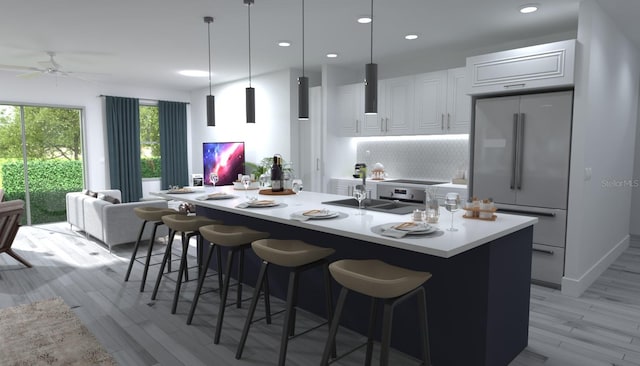 kitchen featuring backsplash, built in refrigerator, a center island with sink, light wood-type flooring, and pendant lighting