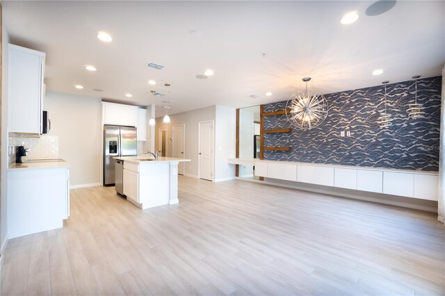 kitchen featuring appliances with stainless steel finishes, backsplash, light hardwood / wood-style floors, a center island with sink, and pendant lighting