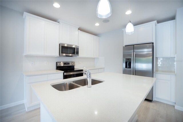 kitchen featuring appliances with stainless steel finishes, light hardwood / wood-style flooring, decorative light fixtures, decorative backsplash, and a center island with sink