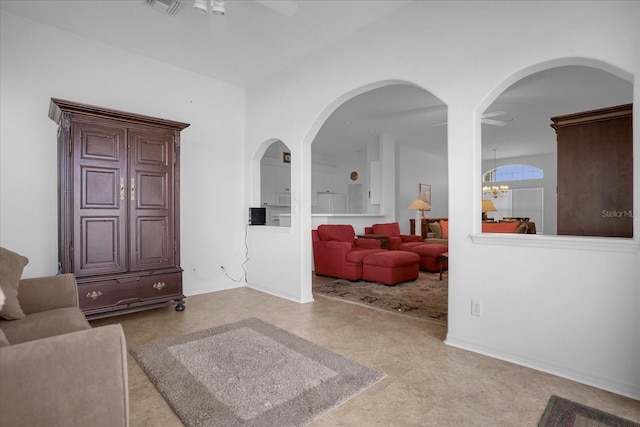 living room featuring ceiling fan with notable chandelier, arched walkways, and baseboards