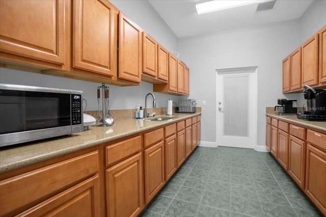 kitchen featuring baseboards, visible vents, stainless steel microwave, light countertops, and a sink