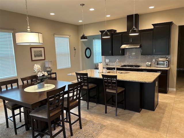 kitchen with sink, tasteful backsplash, light tile patterned floors, a breakfast bar area, and a center island with sink