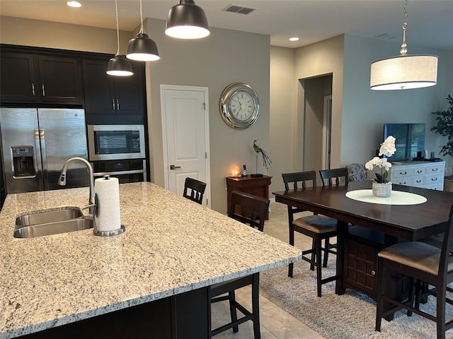 kitchen with sink, light tile patterned floors, a breakfast bar area, stainless steel appliances, and a center island with sink