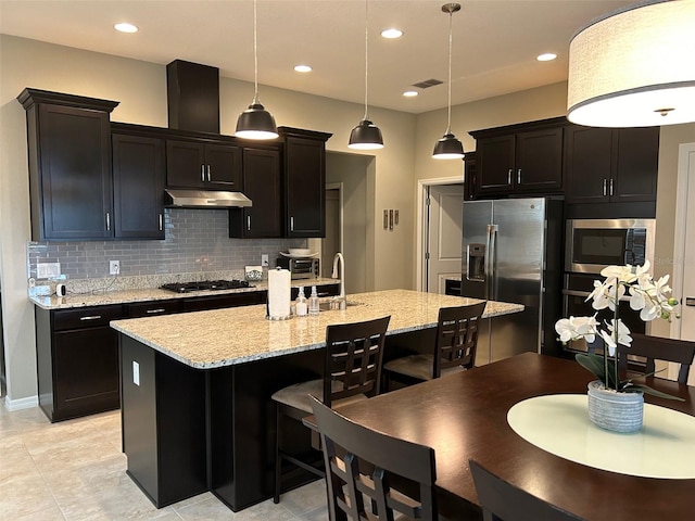 kitchen featuring decorative backsplash, hanging light fixtures, an island with sink, light tile patterned floors, and stainless steel appliances