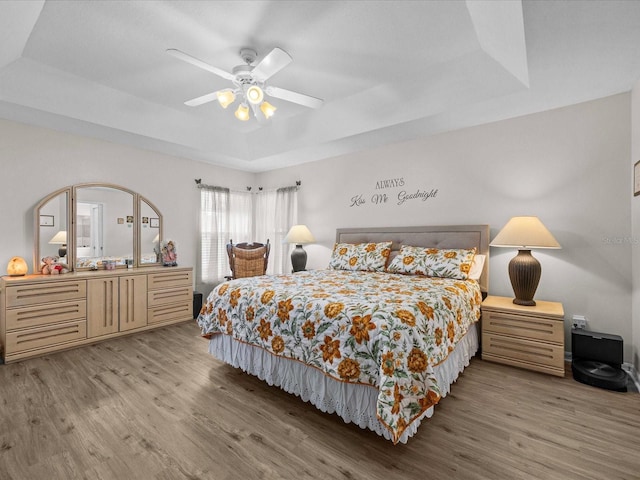 bedroom featuring ceiling fan, a tray ceiling, and light hardwood / wood-style floors