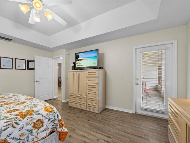 bedroom featuring a raised ceiling, dark hardwood / wood-style floors, access to exterior, and ceiling fan