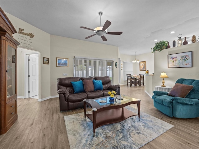 living room featuring ceiling fan with notable chandelier and light hardwood / wood-style flooring