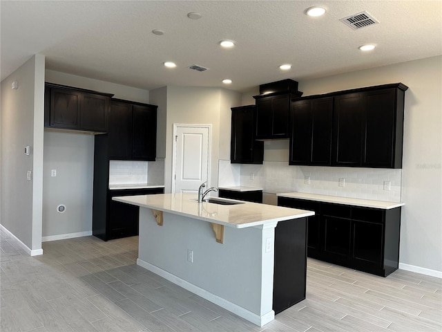 kitchen featuring backsplash, sink, and a kitchen island with sink