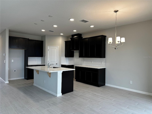 kitchen featuring sink, tasteful backsplash, pendant lighting, a chandelier, and a center island with sink