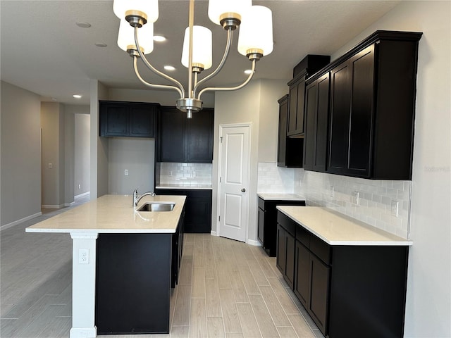 kitchen with a kitchen island with sink, an inviting chandelier, sink, decorative backsplash, and decorative light fixtures