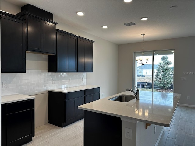 kitchen with a center island with sink, sink, light hardwood / wood-style flooring, decorative light fixtures, and a chandelier