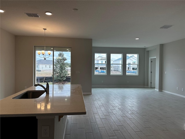 kitchen featuring plenty of natural light, a kitchen island with sink, sink, a chandelier, and hanging light fixtures