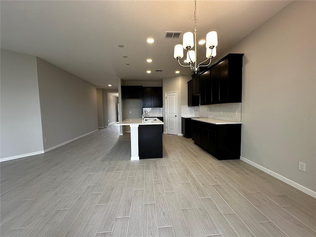 kitchen with tasteful backsplash, an island with sink, light hardwood / wood-style floors, and an inviting chandelier