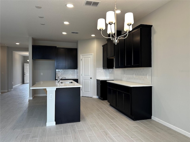 kitchen featuring sink, light wood-type flooring, a kitchen island with sink, and an inviting chandelier