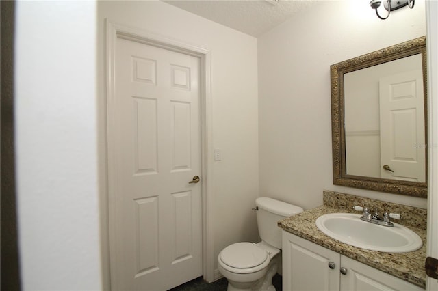 half bathroom featuring toilet, a textured ceiling, and vanity