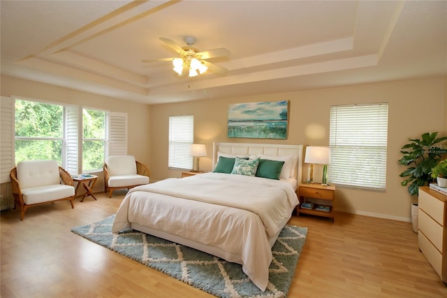 bedroom with baseboards, ceiling fan, a tray ceiling, and light wood-style floors