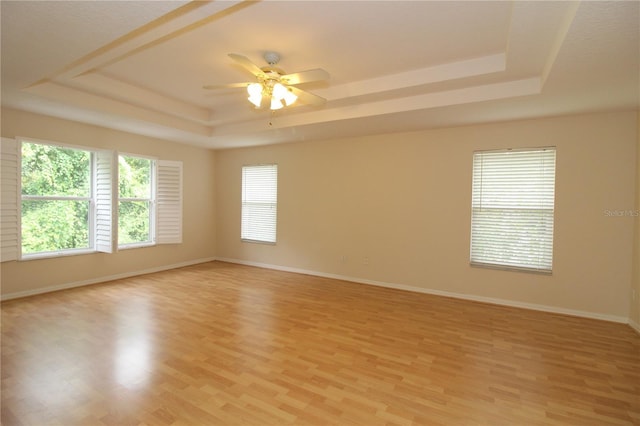 unfurnished room with light wood-style floors, a tray ceiling, and baseboards