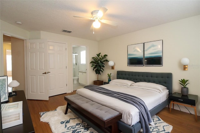 bedroom featuring a textured ceiling, wood finished floors, visible vents, a ceiling fan, and ensuite bath