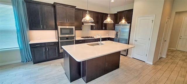 kitchen with pendant lighting, a kitchen island with sink, sink, light hardwood / wood-style floors, and stainless steel appliances