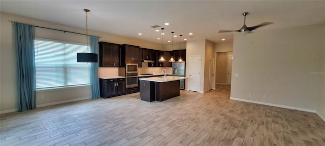 kitchen featuring a center island with sink, appliances with stainless steel finishes, pendant lighting, light hardwood / wood-style floors, and backsplash