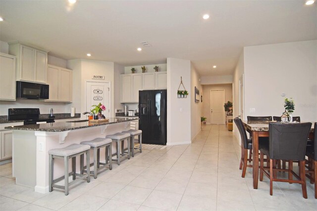 kitchen featuring a breakfast bar area, black appliances, a kitchen island with sink, sink, and dark stone counters