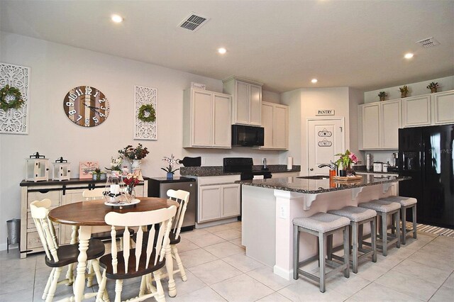 kitchen featuring sink, black appliances, dark stone counters, a kitchen breakfast bar, and a center island with sink