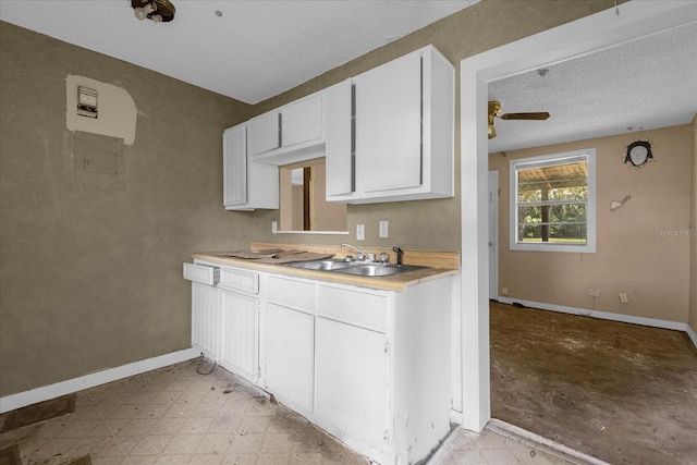 kitchen featuring ceiling fan, a textured ceiling, sink, and white cabinetry