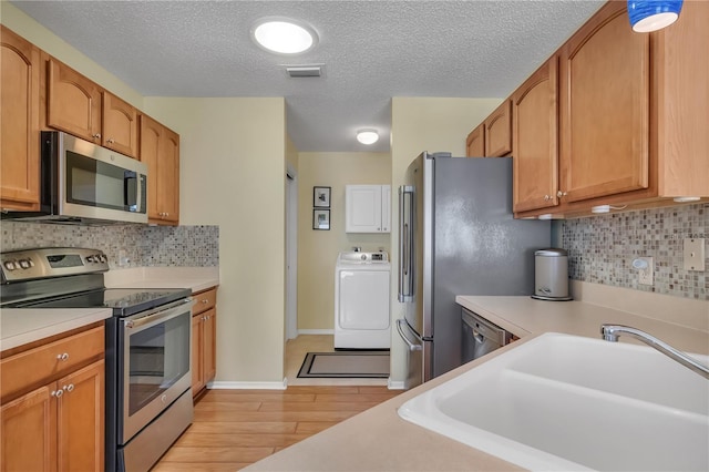 kitchen with sink, light hardwood / wood-style flooring, decorative backsplash, washer / clothes dryer, and stainless steel appliances