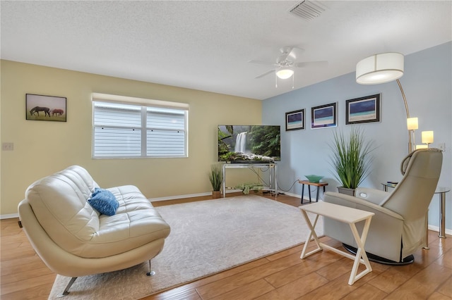 living room featuring ceiling fan, a textured ceiling, and light hardwood / wood-style floors