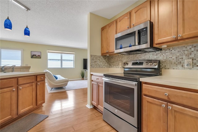 kitchen featuring appliances with stainless steel finishes, light hardwood / wood-style floors, a textured ceiling, and backsplash