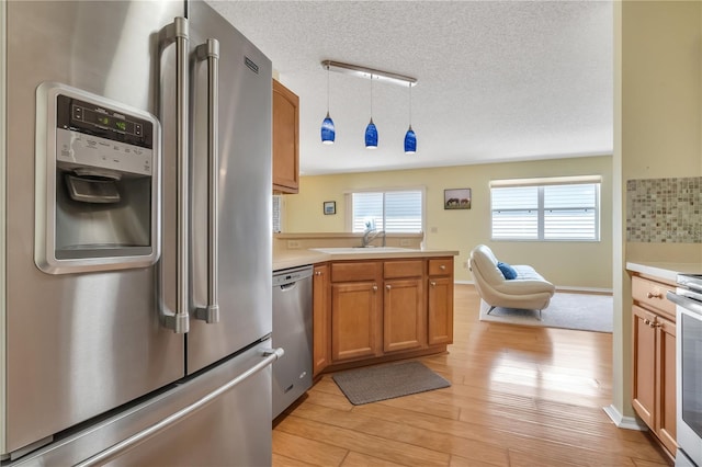 kitchen featuring light wood-type flooring, tasteful backsplash, appliances with stainless steel finishes, sink, and a textured ceiling