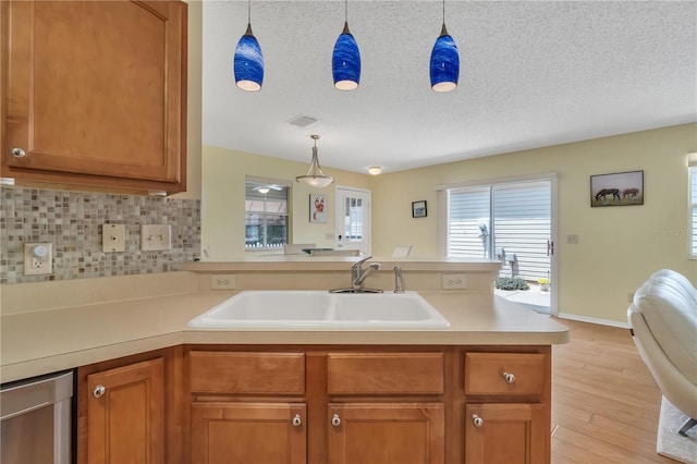 kitchen featuring sink, light hardwood / wood-style flooring, decorative backsplash, a textured ceiling, and kitchen peninsula