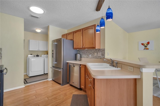 kitchen featuring washing machine and clothes dryer, light hardwood / wood-style flooring, appliances with stainless steel finishes, sink, and a textured ceiling