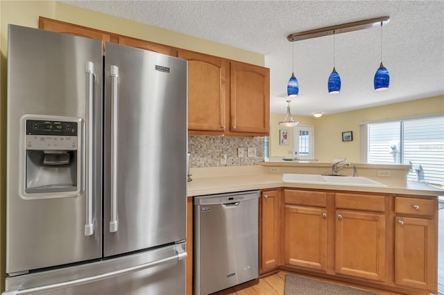 kitchen with decorative backsplash, pendant lighting, appliances with stainless steel finishes, sink, and kitchen peninsula