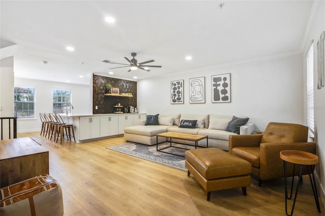 living room with light hardwood / wood-style floors, ornamental molding, and ceiling fan