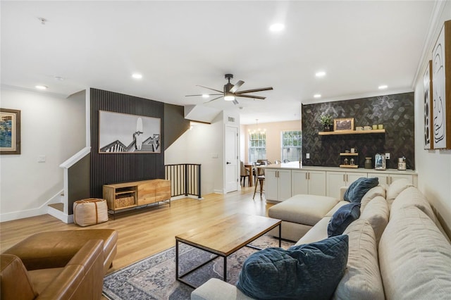 living room with light wood-type flooring, ceiling fan with notable chandelier, and ornamental molding