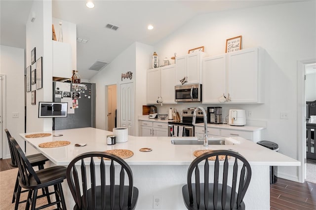 kitchen featuring stainless steel appliances, white cabinetry, dark hardwood / wood-style floors, a kitchen breakfast bar, and vaulted ceiling