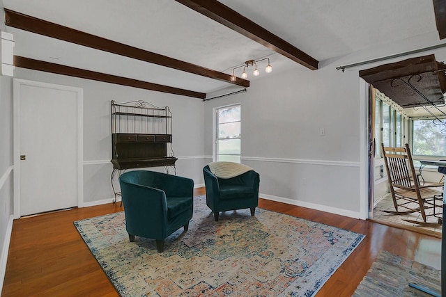 living area featuring a healthy amount of sunlight, beam ceiling, baseboards, and wood finished floors