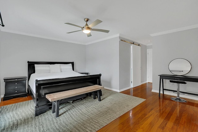 bedroom with a barn door, wood finished floors, a ceiling fan, baseboards, and crown molding