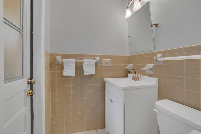 half bath featuring wainscoting, vanity, toilet, and tile walls