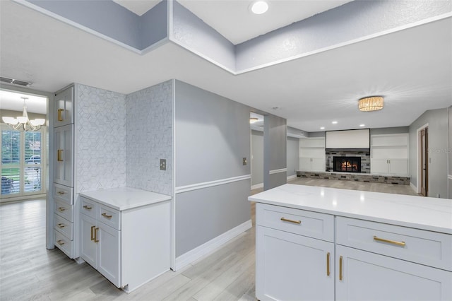 kitchen with light stone countertops, light hardwood / wood-style flooring, decorative backsplash, white cabinetry, and a chandelier