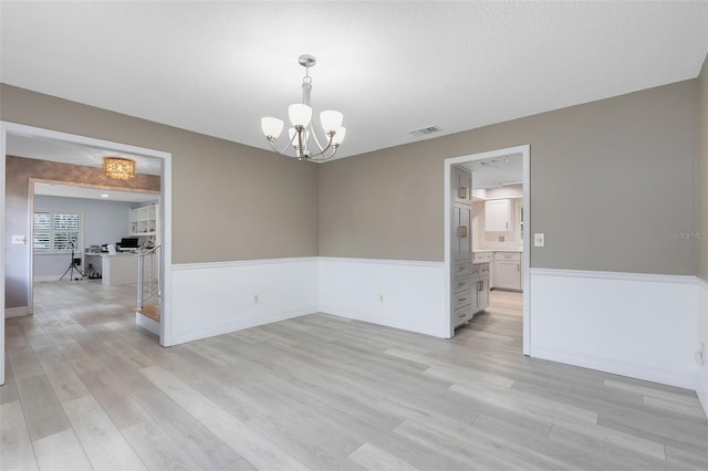 unfurnished room featuring a textured ceiling, light hardwood / wood-style flooring, and a chandelier