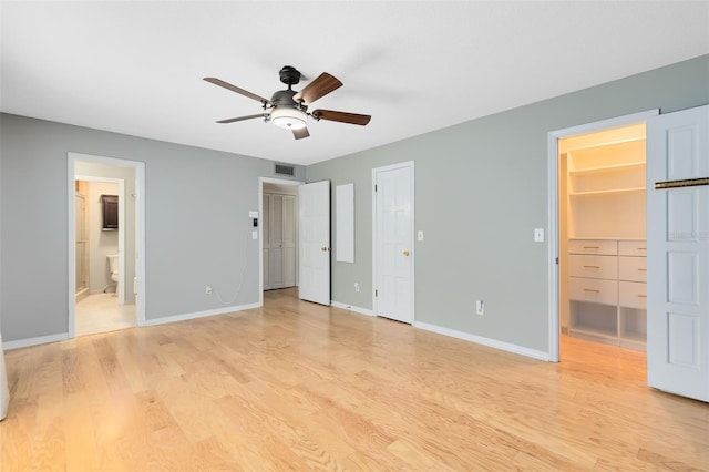 unfurnished bedroom with ceiling fan, light wood-type flooring, a spacious closet, and ensuite bathroom