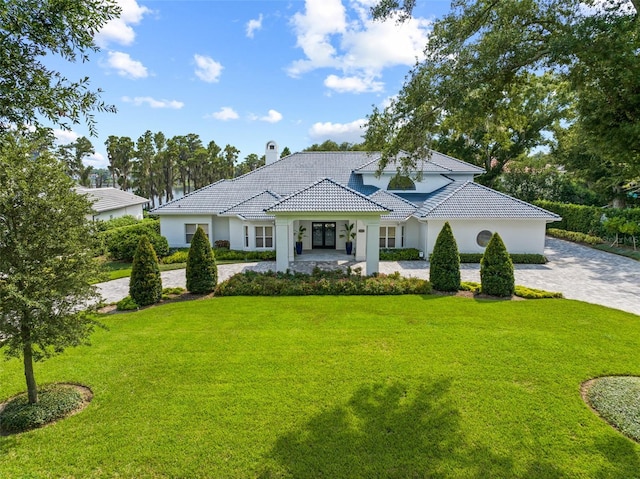 view of front of home featuring a chimney, a tiled roof, decorative driveway, a front lawn, and stucco siding