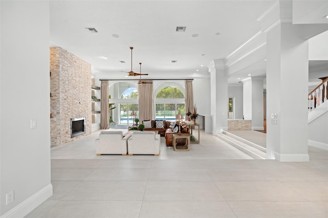 living room featuring ceiling fan, ornate columns, a stone fireplace, and light tile patterned floors